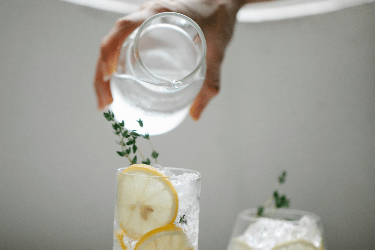 A person pouring water into a glass with lemon and thyme