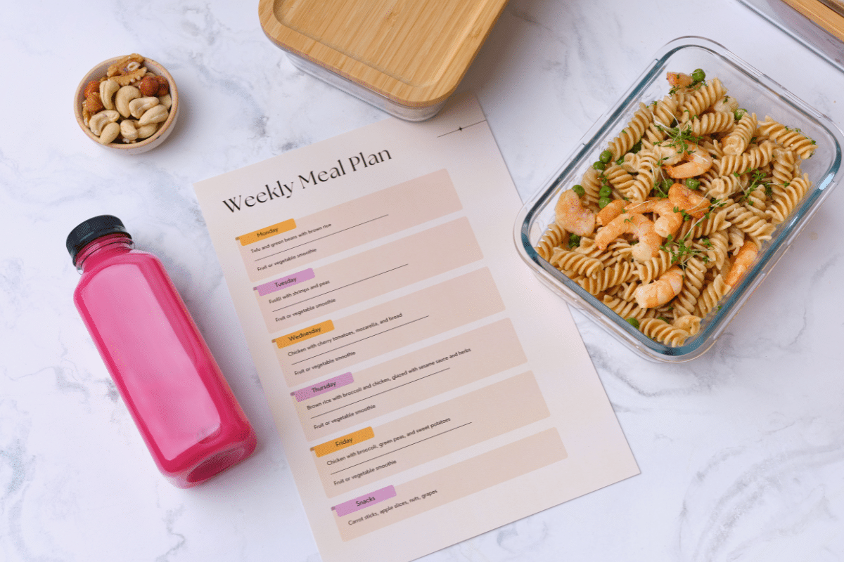 a weekly meal plan on a table and next to it is pasta in a glass container and a water bottle and a bowl with nuts