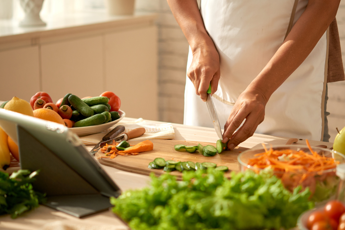 a woman in her kitchen cutting cucumbers on a cutting board there are also other vegetables 