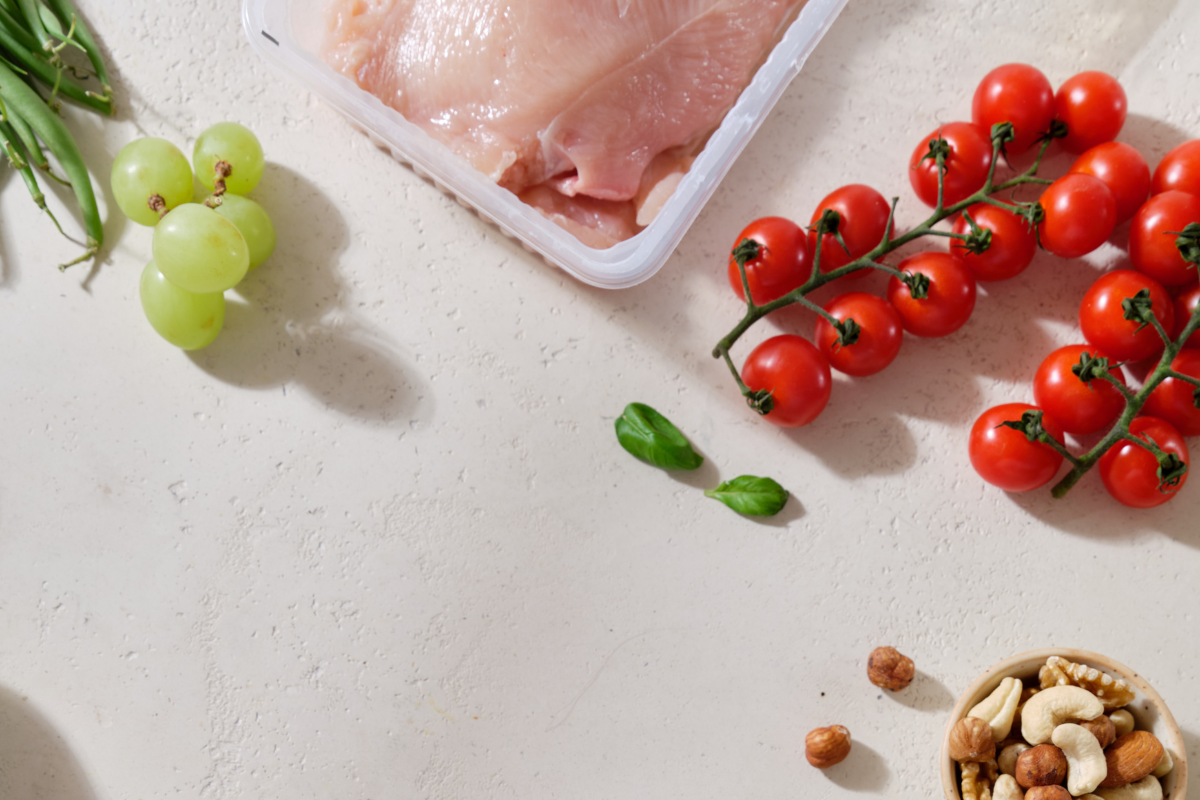 a chicken breast, tomatos, nutas and grapes all on a table 