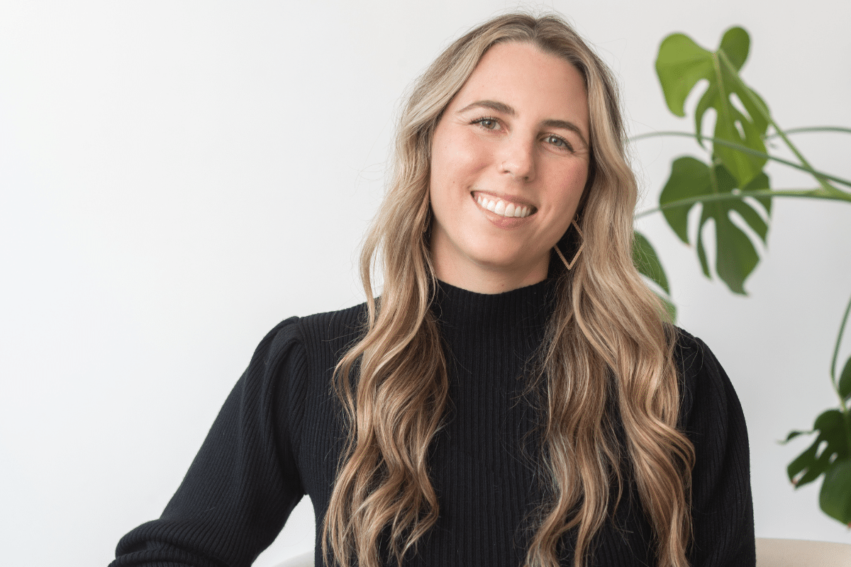 Kate Brock, a HAES dietitian, sitting on a chair in front of a plant in her office